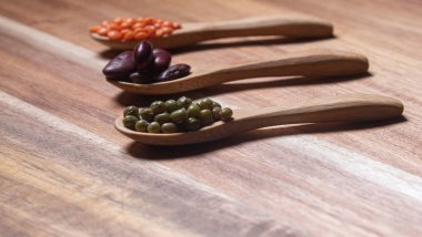 Legumes of different types such as red lentil, green soybean and bean on wooden background