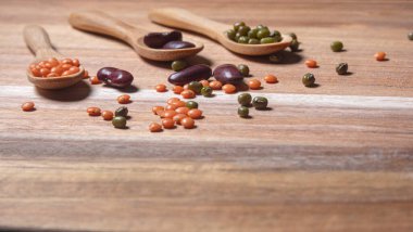 Legumes of different types such as red lentil, green soybean and bean on wooden background