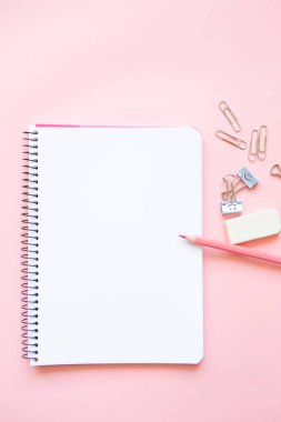 pink pencil and stationery items on notepad with blank page and on pink background