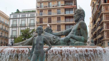 Ancient stone statues in a typical fountain with water in the city of Valencia