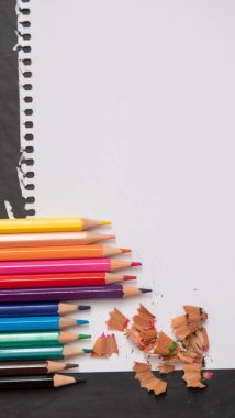 blank page of a notebook as a mock up next to pencils of different colors on a black chalkboard background