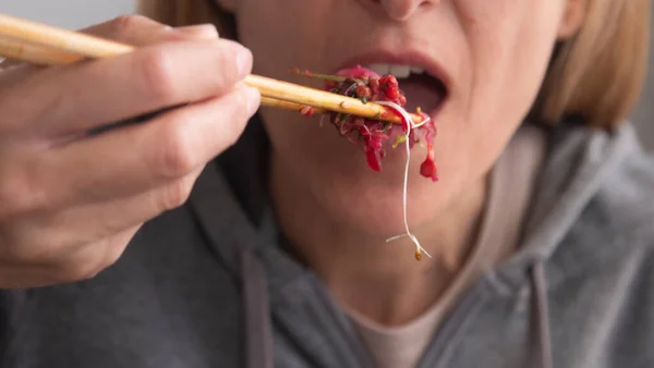 Woman\'s mouth eating sprout salad with chopsticks
