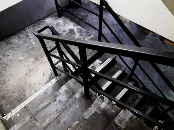 this emergency staircase has a gray cement floor with black iron handrails and neon lights for lighting it looks clean and in good condition