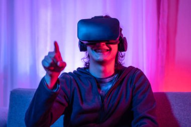 Young man wearing virtual reality (VR) glasses is playing games in a room with red and blue lights, playing a 3D game with excitement, Future games, Gadgets, Technology, VR game concept.