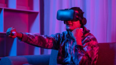 Young man wearing virtual reality (VR) glasses and uses joystick to play games with fun playing games in a room with red and blue lights, 3D game, Future games, Gadgets, Technology, Game concept. 