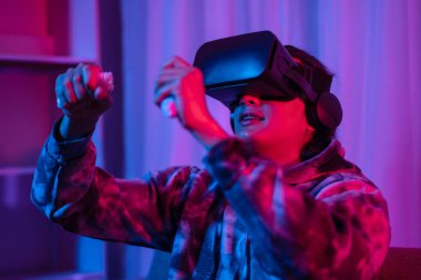 Young man wearing virtual reality (VR) glasses and uses joystick to play games with fun playing games in a room with red and blue lights, 3D game, Future games, Gadgets, Technology, Game concept. 