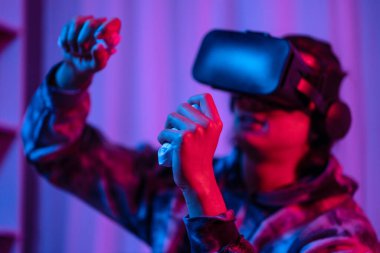 Young man wearing virtual reality (VR) glasses and uses joystick to play games with fun playing games in a room with red and blue lights, 3D game, Future games, Gadgets, Technology, Game concept. 