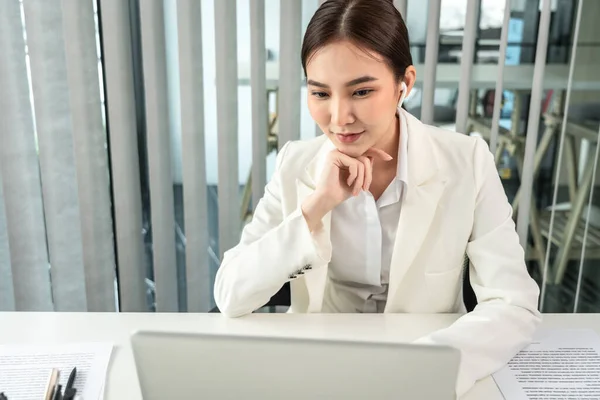 Asian businesswoman uses a laptop to analyze a company\'s financial business graph, Using a laptop for telecommunication work, Happy woman working in front of laptop screen, Modern private office room.