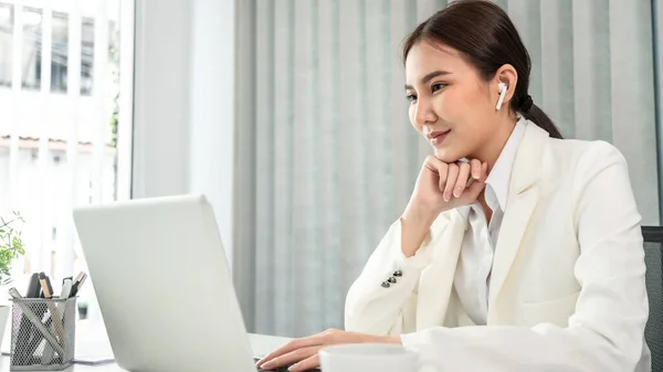 Asian businesswoman uses a laptop to analyze a company\'s financial business graph, Using a laptop for telecommunication work, Happy woman working in front of laptop screen, Modern private office room.