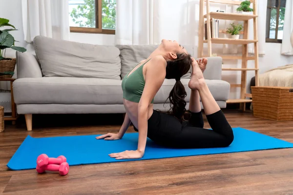 Young woman is practicing yoga with cobra pose during exercise on mat in her living room at home.