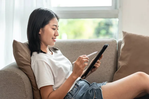 Half-Japanese woman sitting on the sofa using tablet while on vacation, Rest at home, Living room, Relax time, Touch screen tablet, Go on internet, Favorite corner, Personal space.