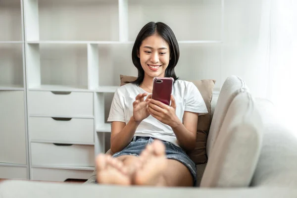 Half-Japanese woman sitting on the sofa using mobile while on vacation, Rest at home, Living room, Relax time, Touch screen tablet, Go on internet, Favorite corner, Personal space.