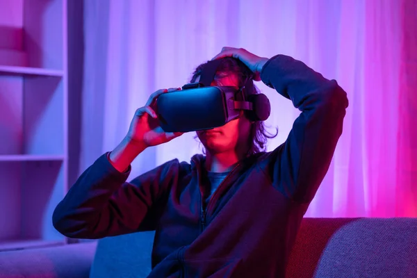 Young man wearing virtual reality (VR) glasses is playing games in a room with red and blue lights, playing a 3D game with excitement, Future games, Gadgets, Technology, VR game concept.