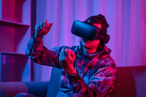 Young man wearing virtual reality (VR) glasses and uses joystick to play games with fun playing games in a room with red and blue lights, 3D game, Future games, Gadgets, Technology, Game concept. 