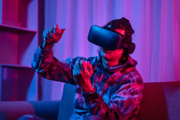 Young man wearing virtual reality (VR) glasses and uses joystick to play games with fun playing games in a room with red and blue lights, 3D game, Future games, Gadgets, Technology, Game concept.