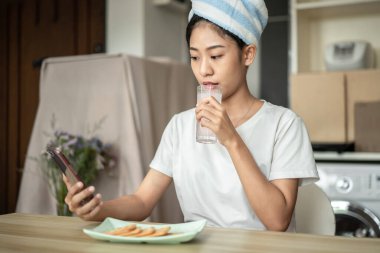 Half Asian woman drinking juice and eating crackers (Healthy whole grain)  for breakfast before going to work, Small room in condominium background, Wake-up activities.