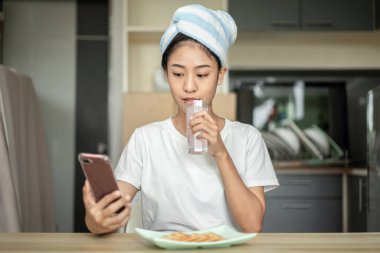 Half Asian woman drinking juice and eating crackers (Healthy whole grain)  for breakfast before going to work, Small room in condominium background, Wake-up activities.