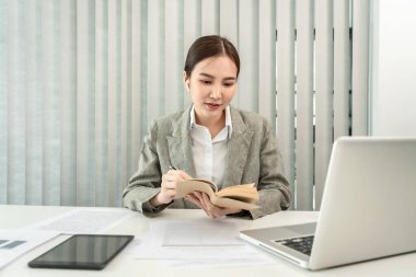Asian businesswoman taking notes in a notebook, Note the main content and details of the main points of the document, Analyzing statistical graph data to improve or develop the organization to grow.