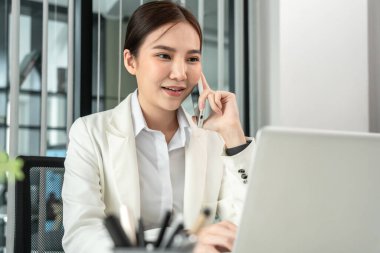 Asian businesswoman talking on the phone and use the laptop to work with a colleague in a private office, Telephone communication, Emote conversation, World of communication technology