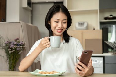 Asian woman eats crackers for breakfast and uses her mobile phone to check the morning news before going to work, Working people's urgent food, Urgent activity after waking up.