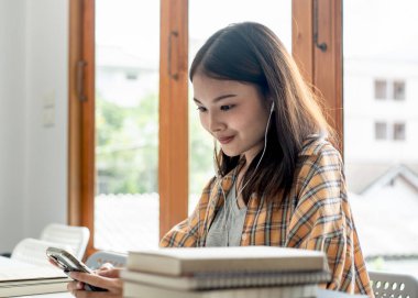 Young woman student in headset is video conference and chatting on smartphone with classmates and lecturer after finished class in college.