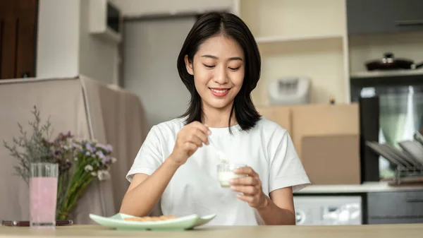 Tanned Asian woman eating yogurt and crackers for breakfast, Health care by eating a diet that is low in fat and calories, The most popular food of the working age, Wake-up activities.