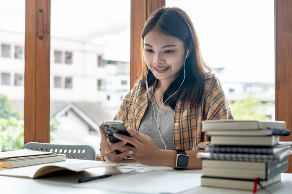 Young woman student in headset is video conference and chatting on smartphone with classmates and lecturer after finished class in college.