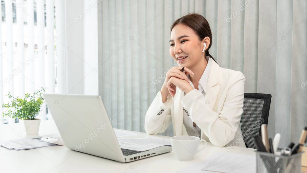 Asian businesswoman talking on the wireless headphones with a colleague in a private office, Telephone communication, Emote conversation, Modern office with laptop and documents on the desk.