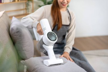 Housekeeper is using cordless vacuum cleaner with handheld for cleanups and vacuuming dirt on furniture in living room while working to perform routine house cleaning.