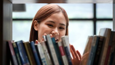 Female student is standing in front of the bookshelf to choosing textbook or literature in library between take a break from studying lessons class at university.