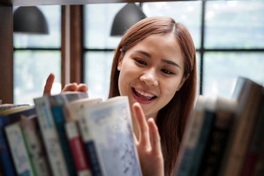 Female student is standing in front of the bookshelf to choosing textbook or literature in library between take a break from studying lessons class at university.