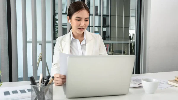 Asian businesswoman uses a laptop to analyze a company\'s financial business graph, Using a laptop for telecommunication work, Happy woman working in front of laptop screen, Modern private office room.