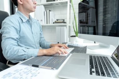 Male programmer is programing to developing program app and website of corporate while working to checking program code and debugging on multiple screen at modern software office.