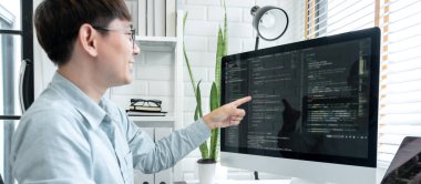Male programmer pointing on screen and programing to developing program app and website of corporate while working to checking program code and debugging on multiple screen at modern software office.