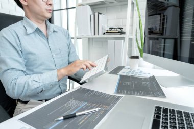 Male programmer is programming to develop program app and website of corporate while working to checking program code and debugging on multiple screen at modern software office.