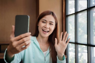 Female student using smartphone to greeting with classmate on video call while studying online learning .