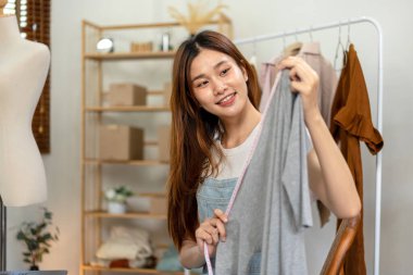 Kadın çevrimiçi satıcı, kıyafetlerin göğüs ölçüsünü ölçerken ve sosyal medyada çevrimiçi kıyafet satarken moda tanıtımı için Vlog üzerinden canlı yayın yapmak üzere dizüstü bilgisayar kullanıyor..