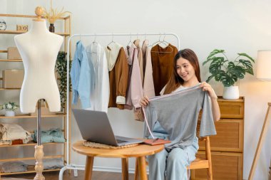 Kadın çevrimiçi satıcı, kıyafetlerin göğüs ölçüsünü ölçerken ve sosyal medyada çevrimiçi kıyafet satarken moda tanıtımı için Vlog üzerinden canlı yayın yapmak üzere dizüstü bilgisayar kullanıyor..