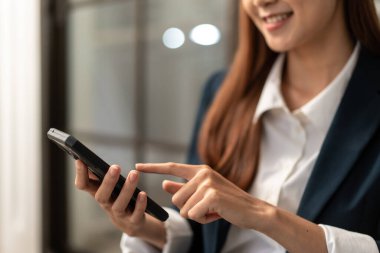 İş kadını, modern ofisteki yeni proje sırasında akıllı telefondan müşteriye e-posta göndermek için finansal raporları ve iş detaylarını okuyor..