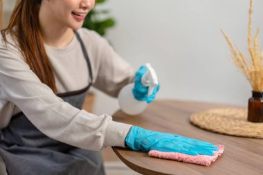 Temizlikçi koruyucu eldiven takıyor ve temizlik için mikrofiber bez kullanıyor ve rutin ev temizliği yaparken masadaki kiri temizliyor..