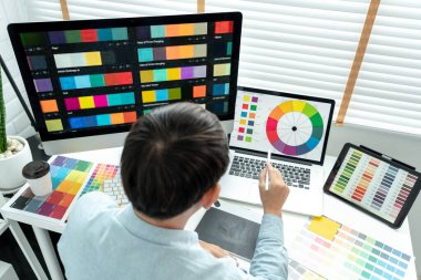 Erkek grafik tasarımcısı birçok ekrandan renk örnekleri seçiyor ve modern ofiste teknolojiyle çalışan grafik tasarımı için tablet dijital üzerinde çizim yapıyor..