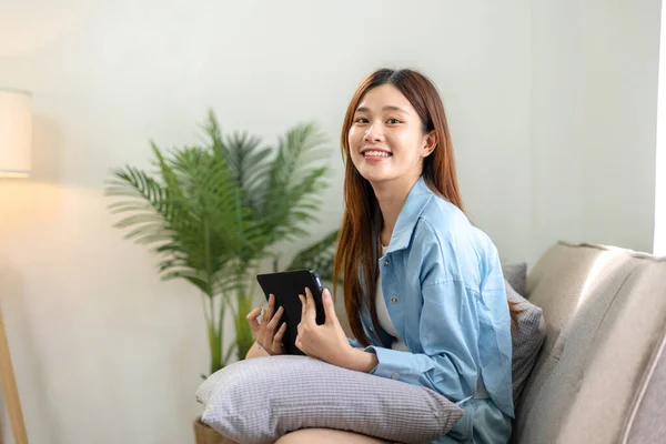 年轻女性在家里客厅舒适的沙发上工作时 正在分析公司的战略目标 并在平板电脑上记笔记 — 图库照片