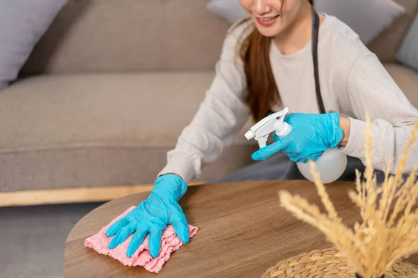 Housekeeper is wear protective gloves and using microfiber cloth with spray cleanser for cleanups and wiping dirt on the desk while working to perform routine house cleaning.