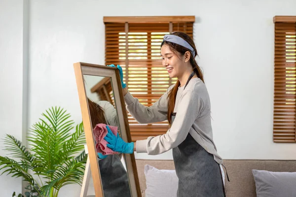 家政婦は保護手袋を着用し 日常的な家の掃除を実行するために働いている間 ガラス上の汚れをきれいにし 拭くためにマイクロファイバー布を使用しています — ストック写真