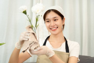 Temizlikçi koruyucu eldiven takıyor ve ev temizliği yaparken cam vazodaki kiri temizlemek için mikrofiber bez kullanıyor..