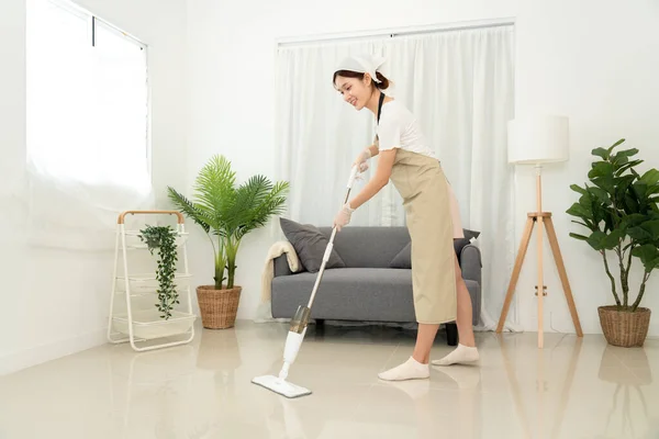Housekeeper is use mop with vacuum cleaner to housekeeping with vacuuming and wiping dirty laminate on the floor in living room while working to perform routine house cleaning.