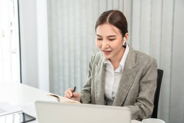 Asian businesswoman taking notes in a notebook, Note the main content and details of the main points of the document, Analyzing statistical graph data to improve or develop the organization to grow.