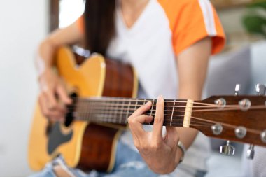 Genç kadın evdeki kanepede rahat bir şekilde otururken gitar çalıyor ve şarkı söylemeye çalışıyor..