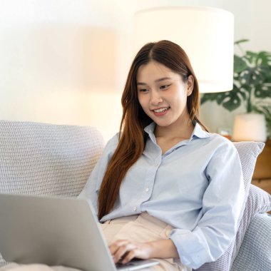 Serbest kadın, iş verilerini okuyup dizüstü bilgisayarda bilgi yazarken aynı zamanda kanepede rahat bir şekilde oturuyor ve merkez ofisteki oturma odasında çalışıyor..