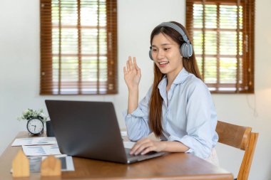 Kadın serbest bilgisayar kullanıyor ve kulaklık takıyor. Çalışma odasında oturma odasındaki masada çalışırken iş arkadaşıyla video konferansına gidiyor..